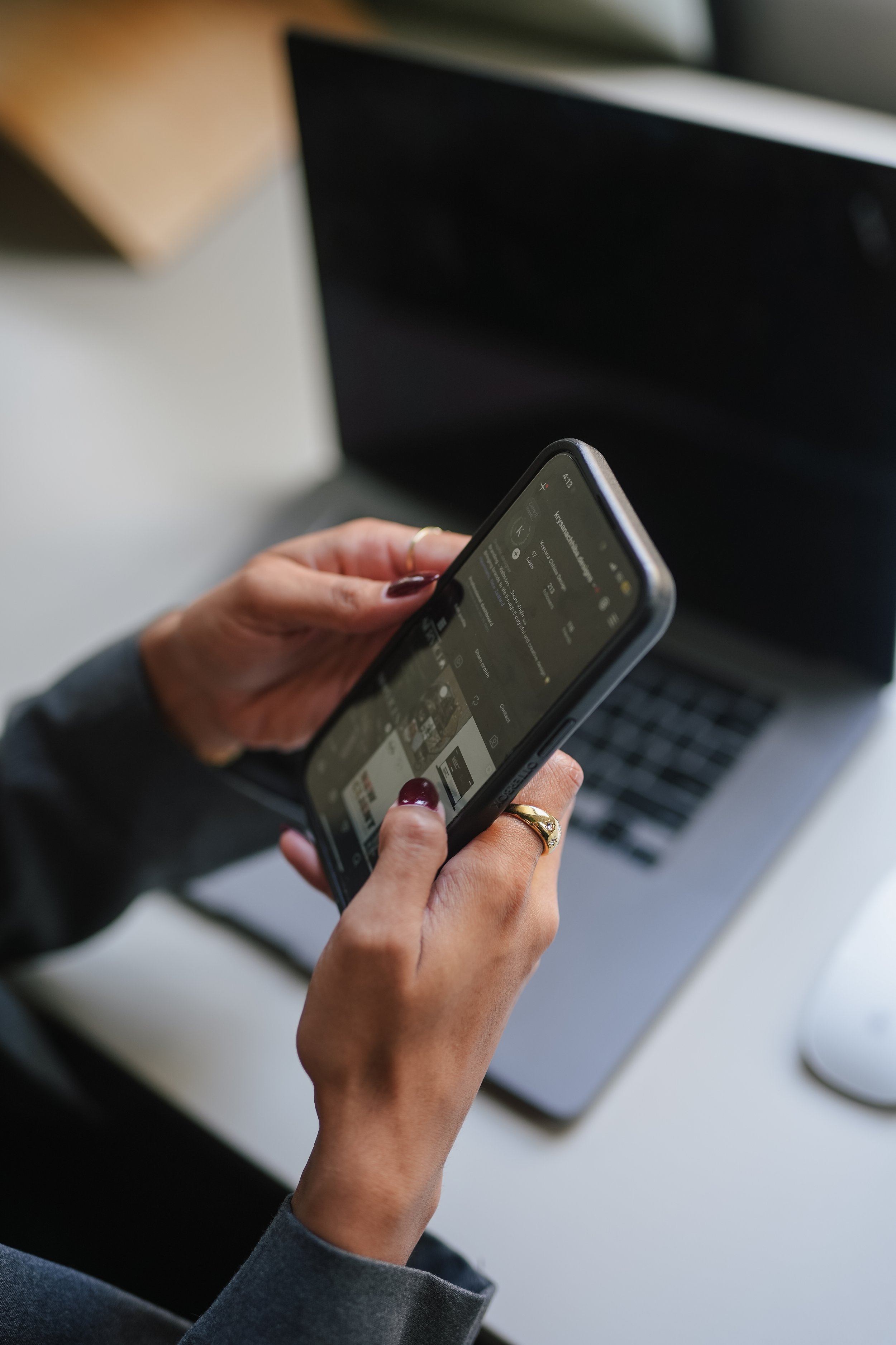 A person holding a smartphone with a search page open, in front of a laptop.