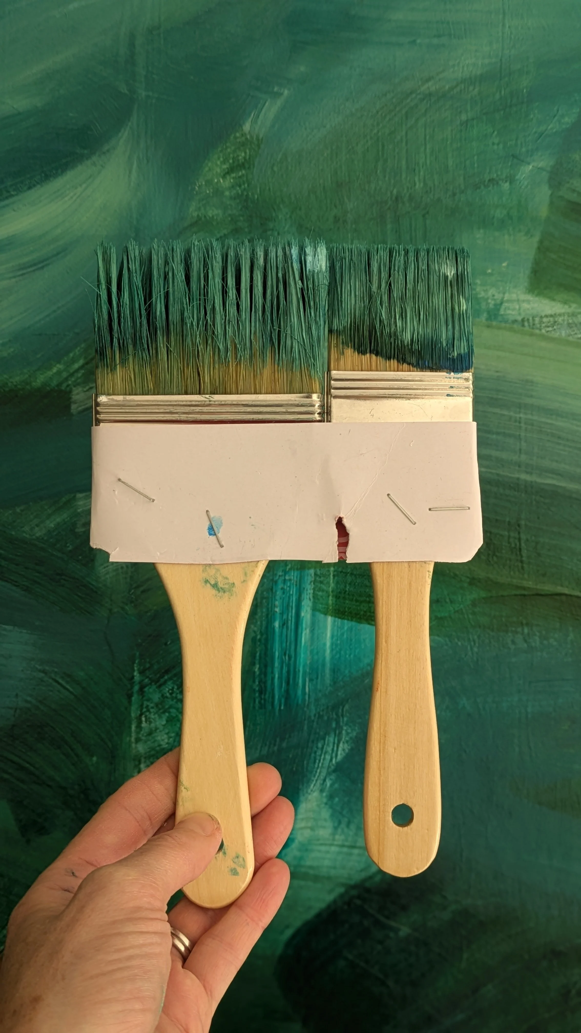 Two paintbrushes held in a hand against a painted green background.