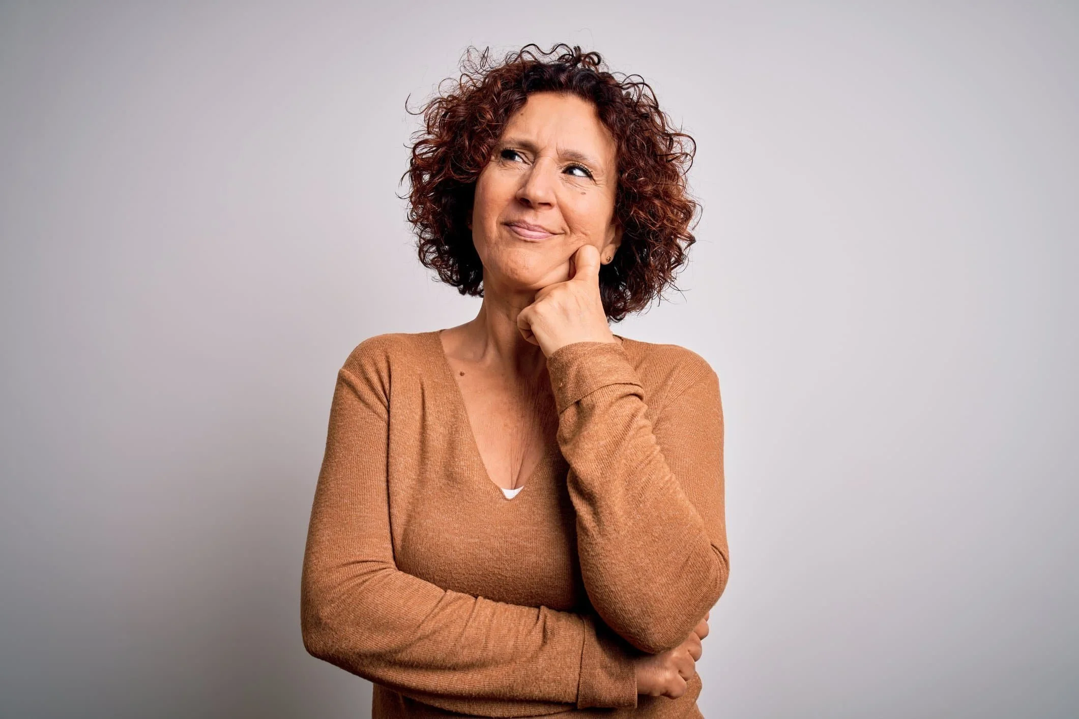 a woman wearing a brown sweater thinks about how to find an agent to help her sign up for Medicare Insurance.