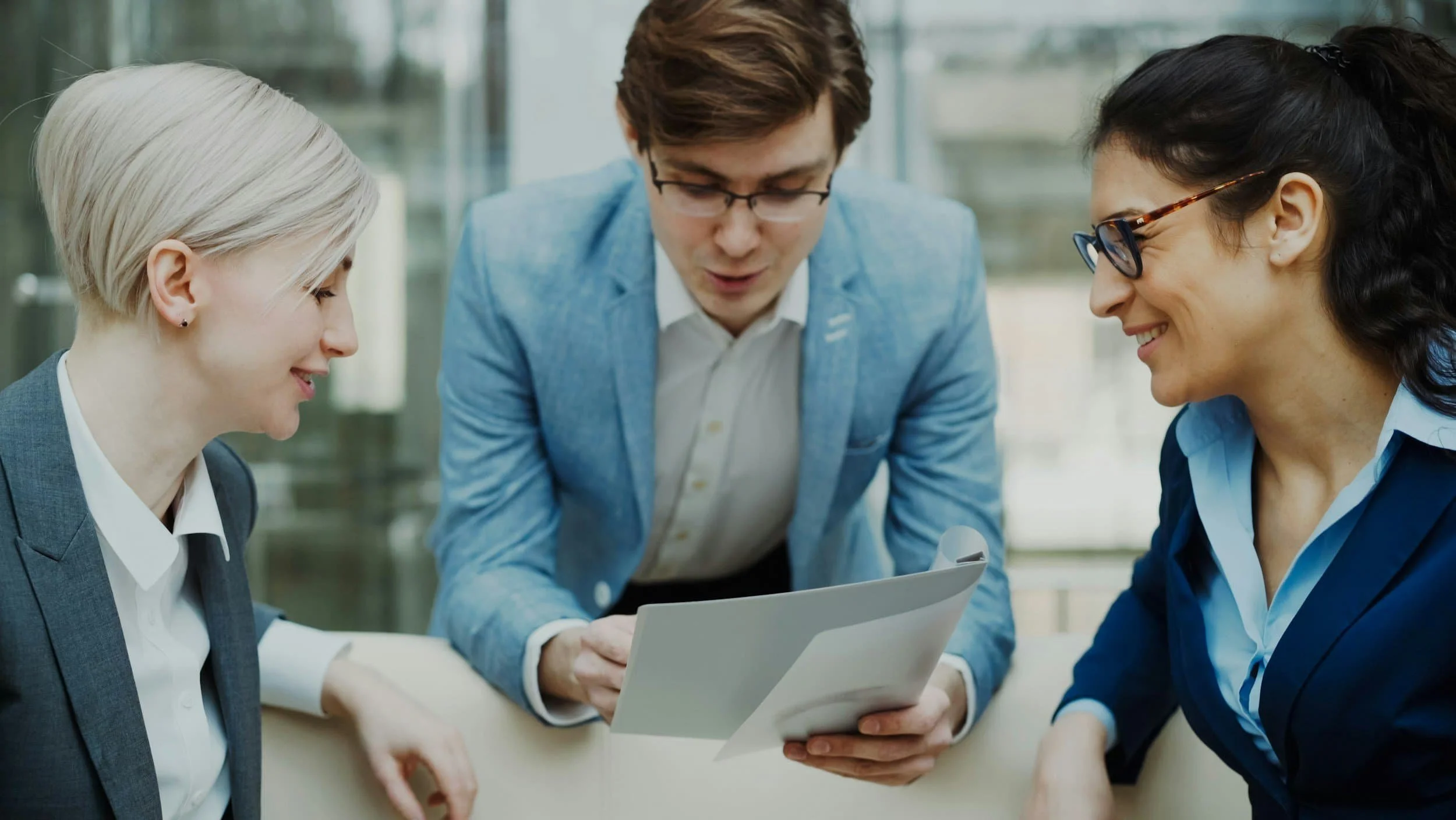 Three professionals in business attire review documents, smiling and engaged at a modern Medicare Insurance Agency office.