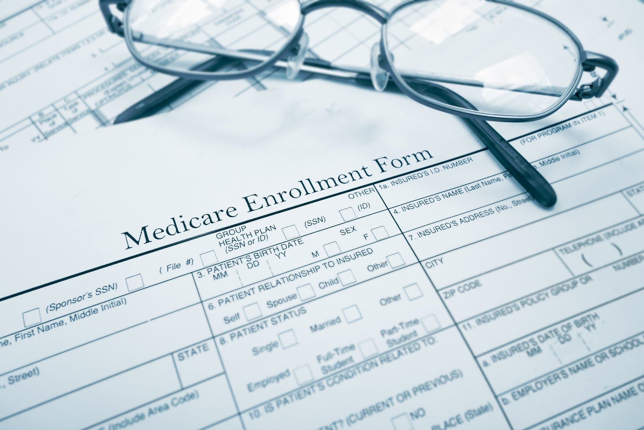 A pair of glasses rests on a Medicare Insurance Enrollment Form with a pen beside them, ready for important decisions.