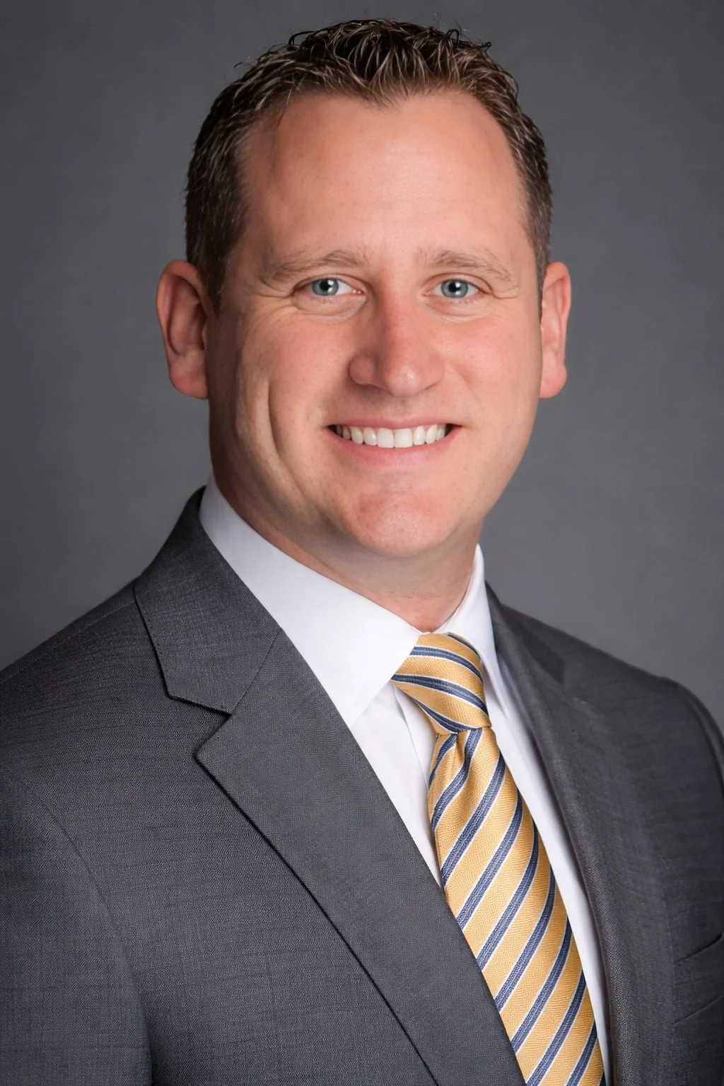 Insurance Agent Jason Kidwell, smiling in a gray suit, white shirt, and yellow striped tie, stands against a gray background.