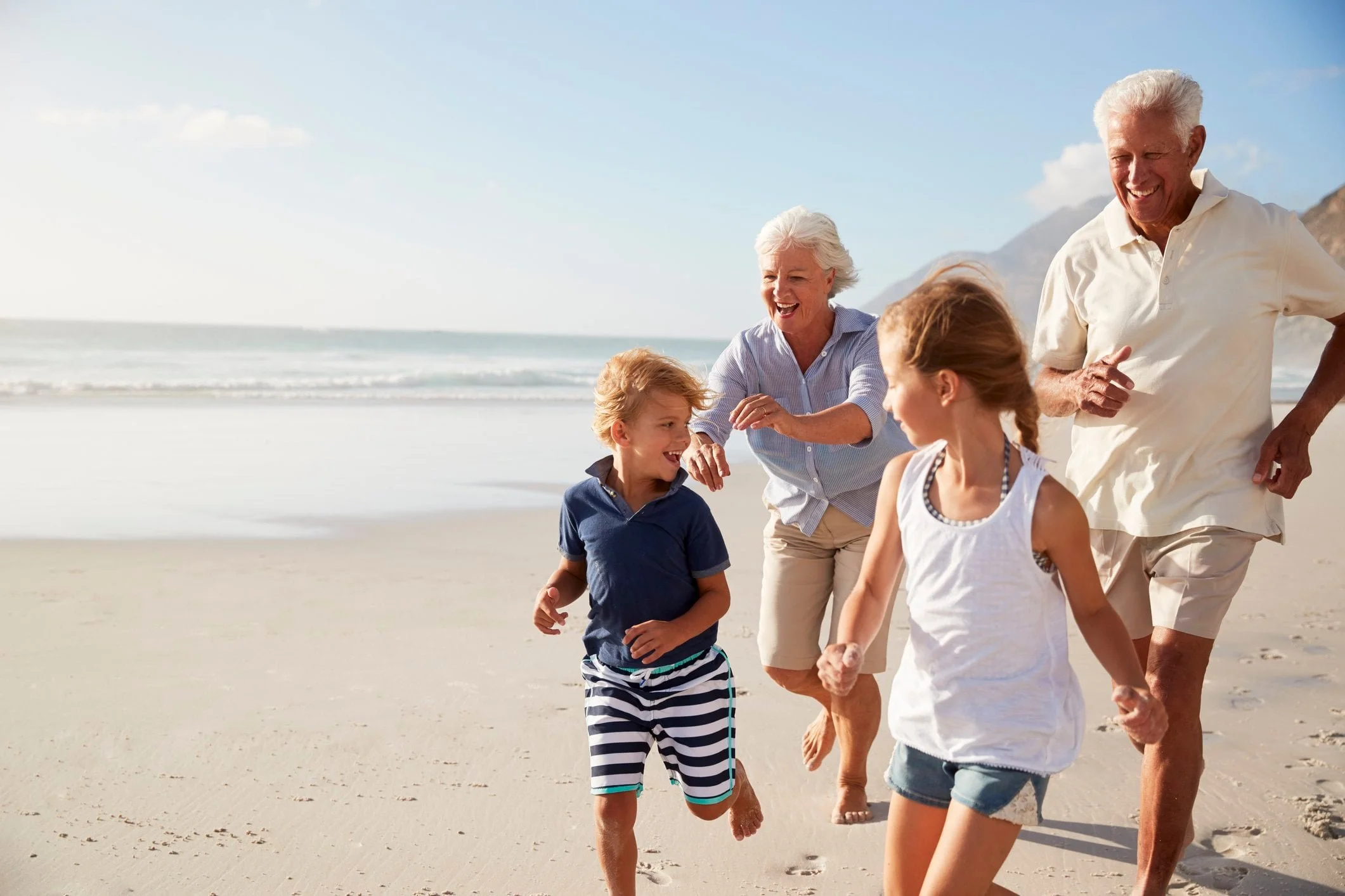 Two seniors and two children laugh and run along a sunny beach, creating memories—Insurance Guidance helps protect such joyful moments.