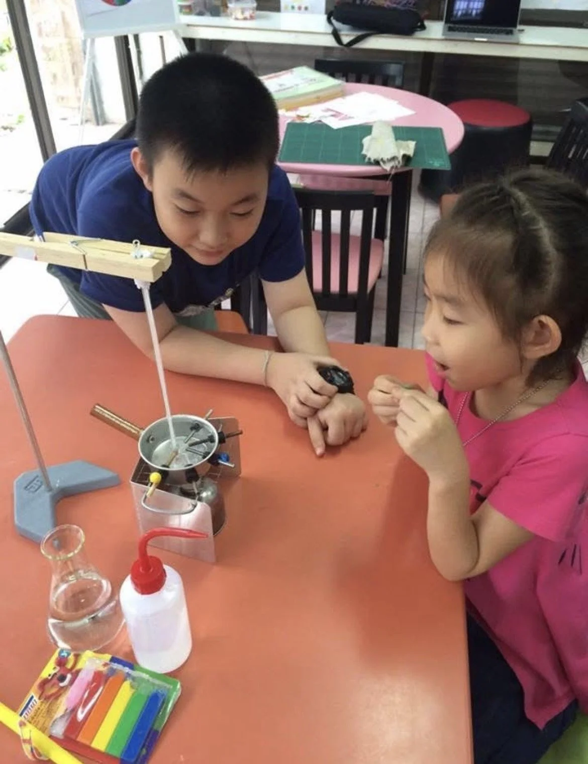 A boy and girl conducting a science experiment with a Bunsen burner and other lab equipment on a table.