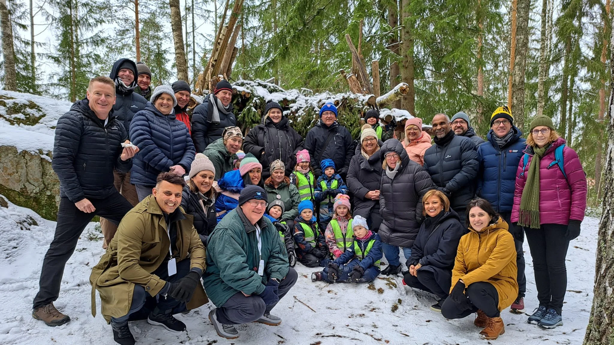 Group of people smiling and posing for a photo in a snowy forest with trees and a fallen log in the background.