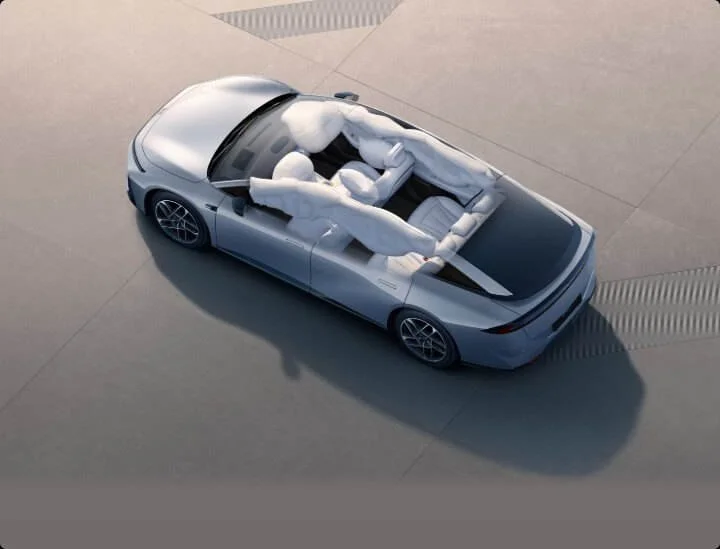 A silver convertible car with white airbags deployed inside, viewed from above on a plain concrete surface.