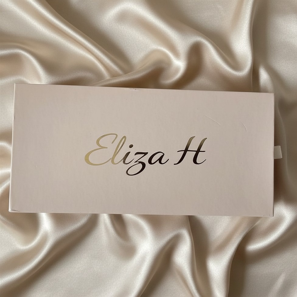 Eliza H luxury gift drawer box in blush pink with gold script logo, presented on ivory silk fabric