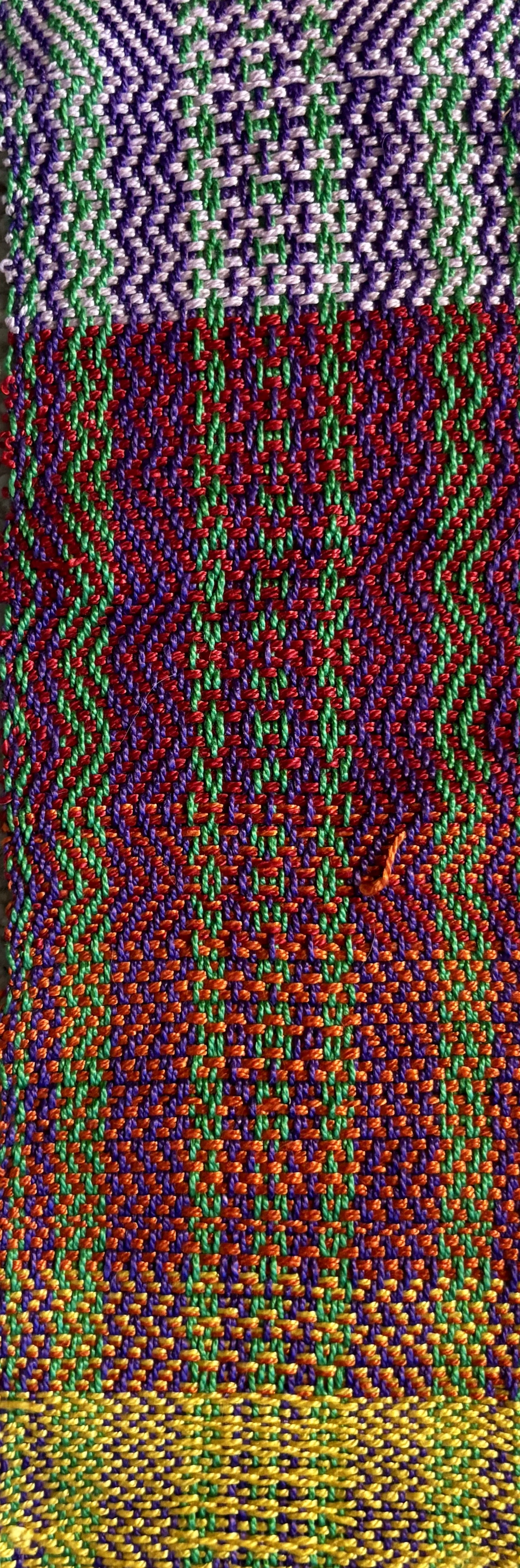 Close-up of colorful woven textile with zigzag and geometric patterns in purple, green, red, yellow, and orange threads.