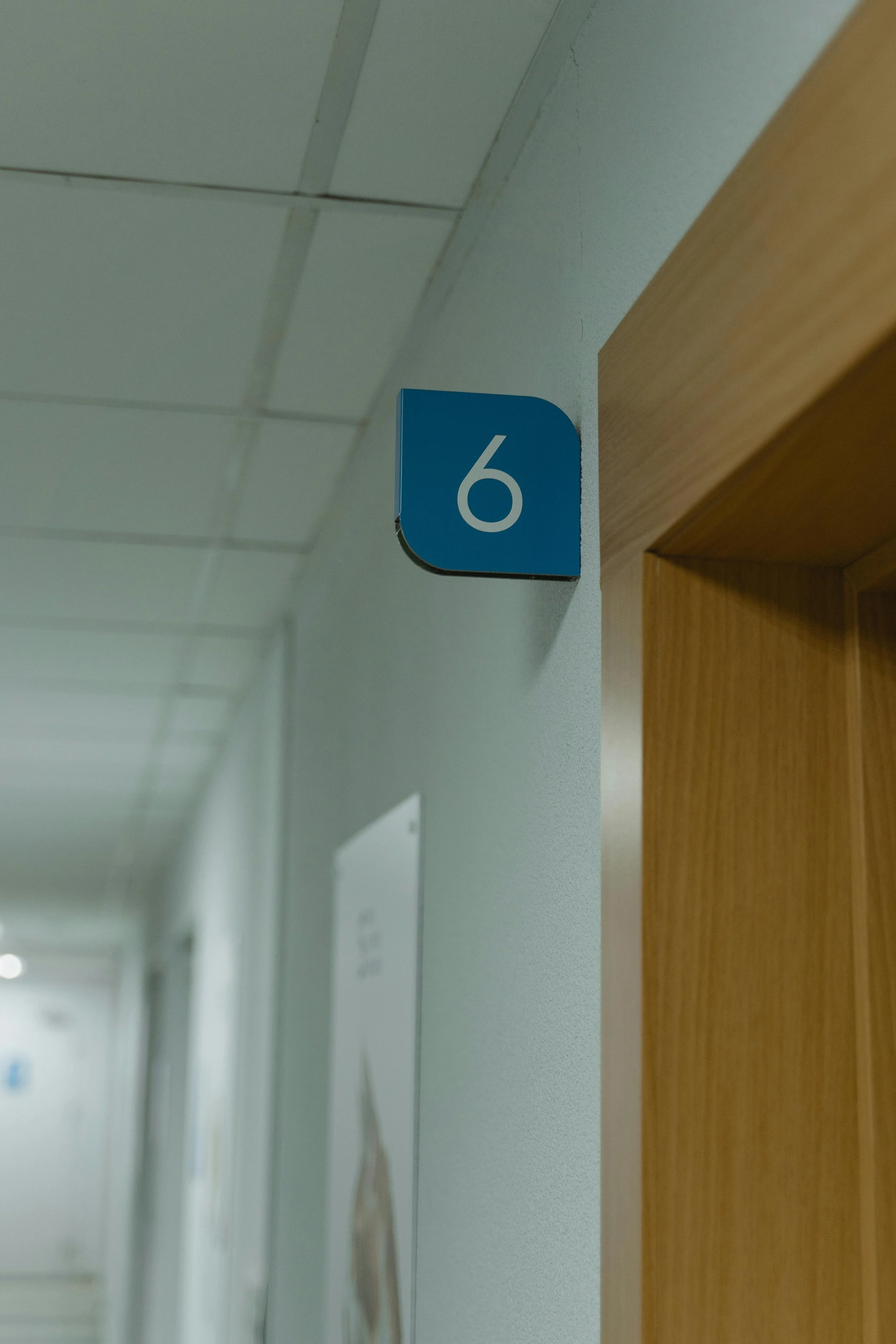 A blue room number sign with the number 6 mounted on a wall next to a wooden doorframe.