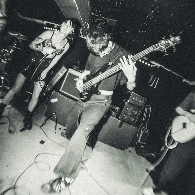 Black and white photo of a band performing live on stage, featuring a female singer and a male guitarist.