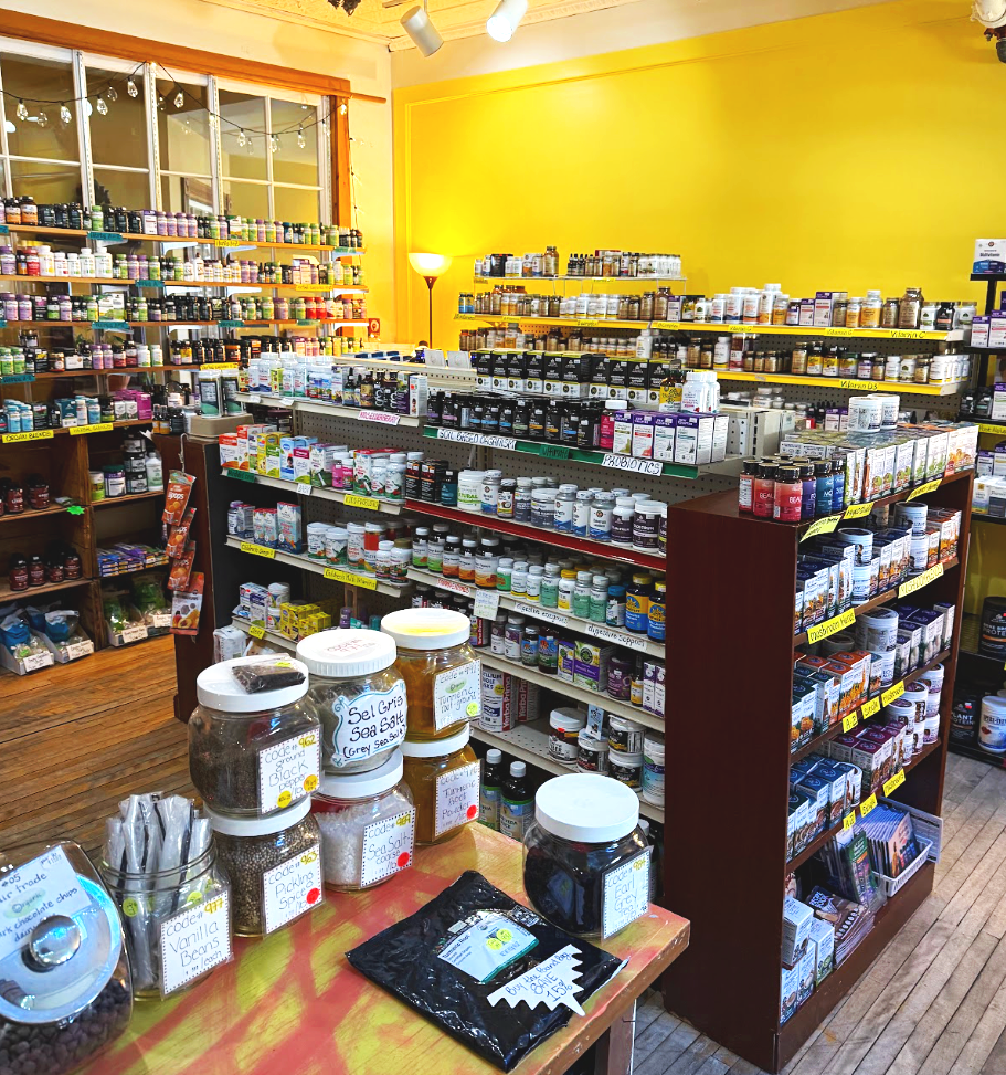 Many shelves filled with supplement bottles, jars, and boxes in a health store, with a yellow wall and wooden flooring.
