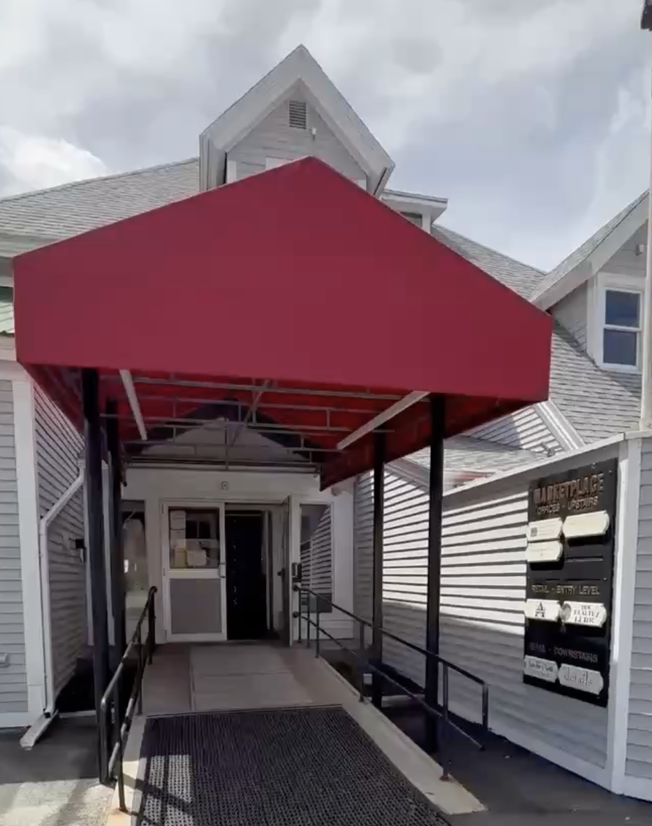 Entrance of a building with a red awning, a ramp, and signs outside.