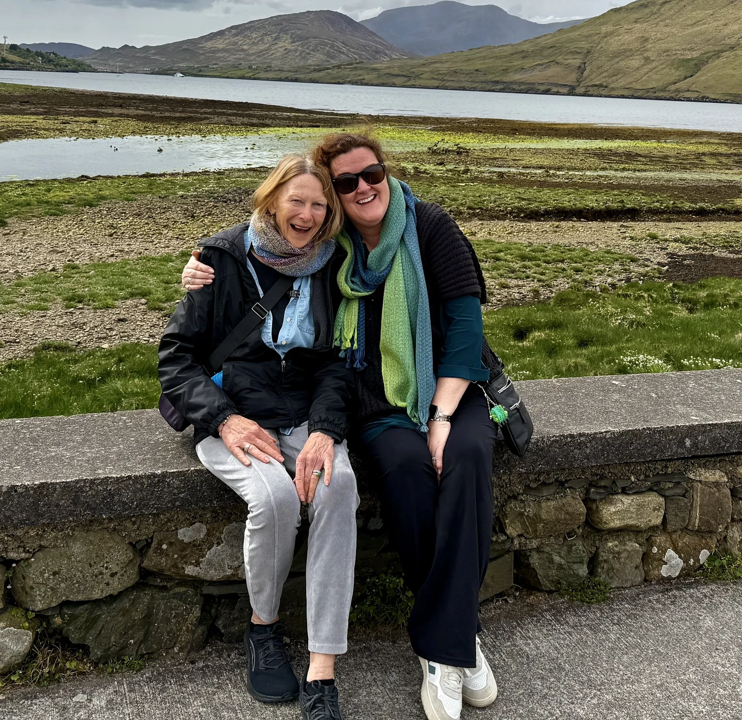 Jennifer and a guest beside a lake with mountains beyond
