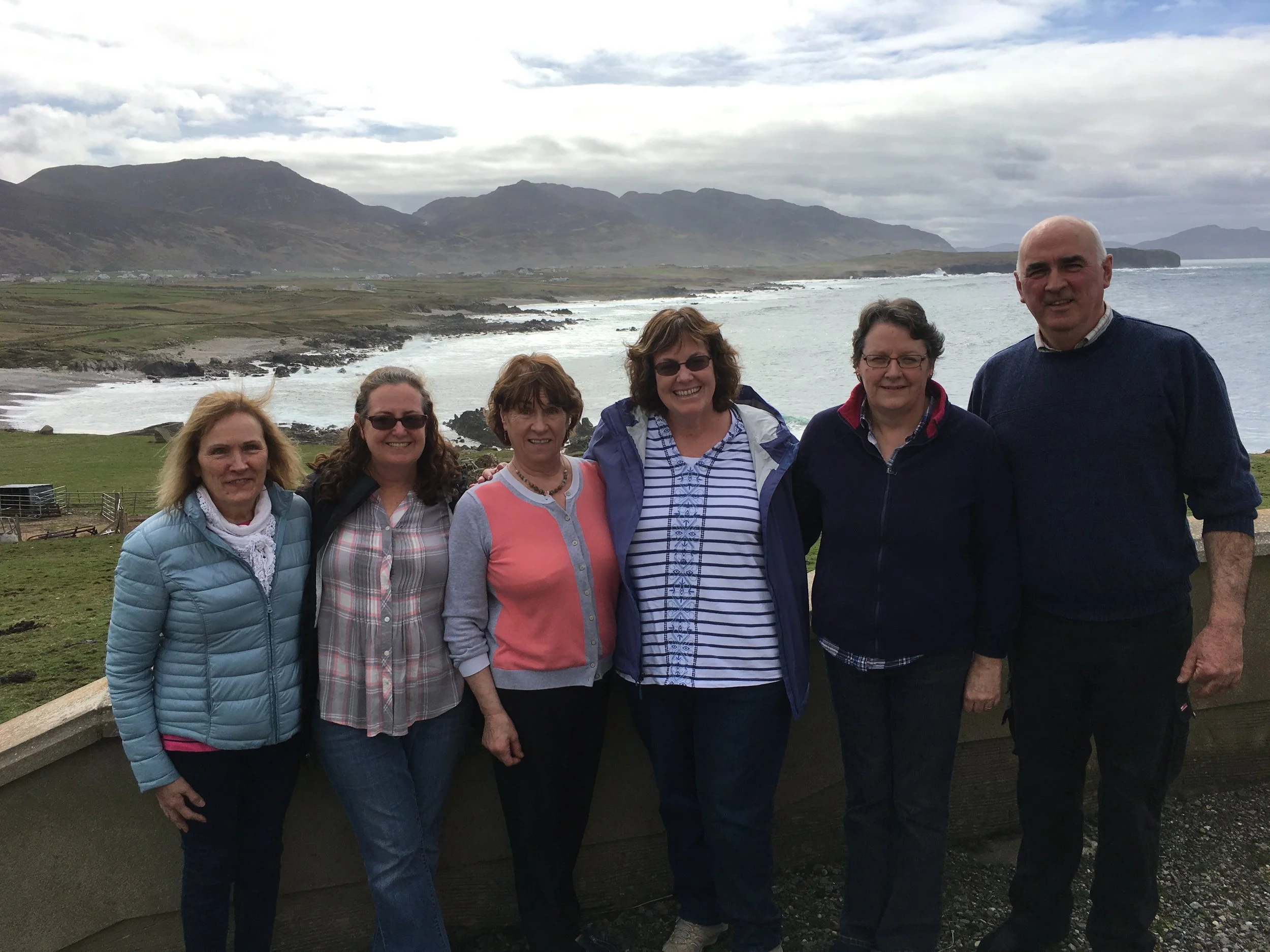 Group of six people standing outdoors with mountains and ocean in the background.