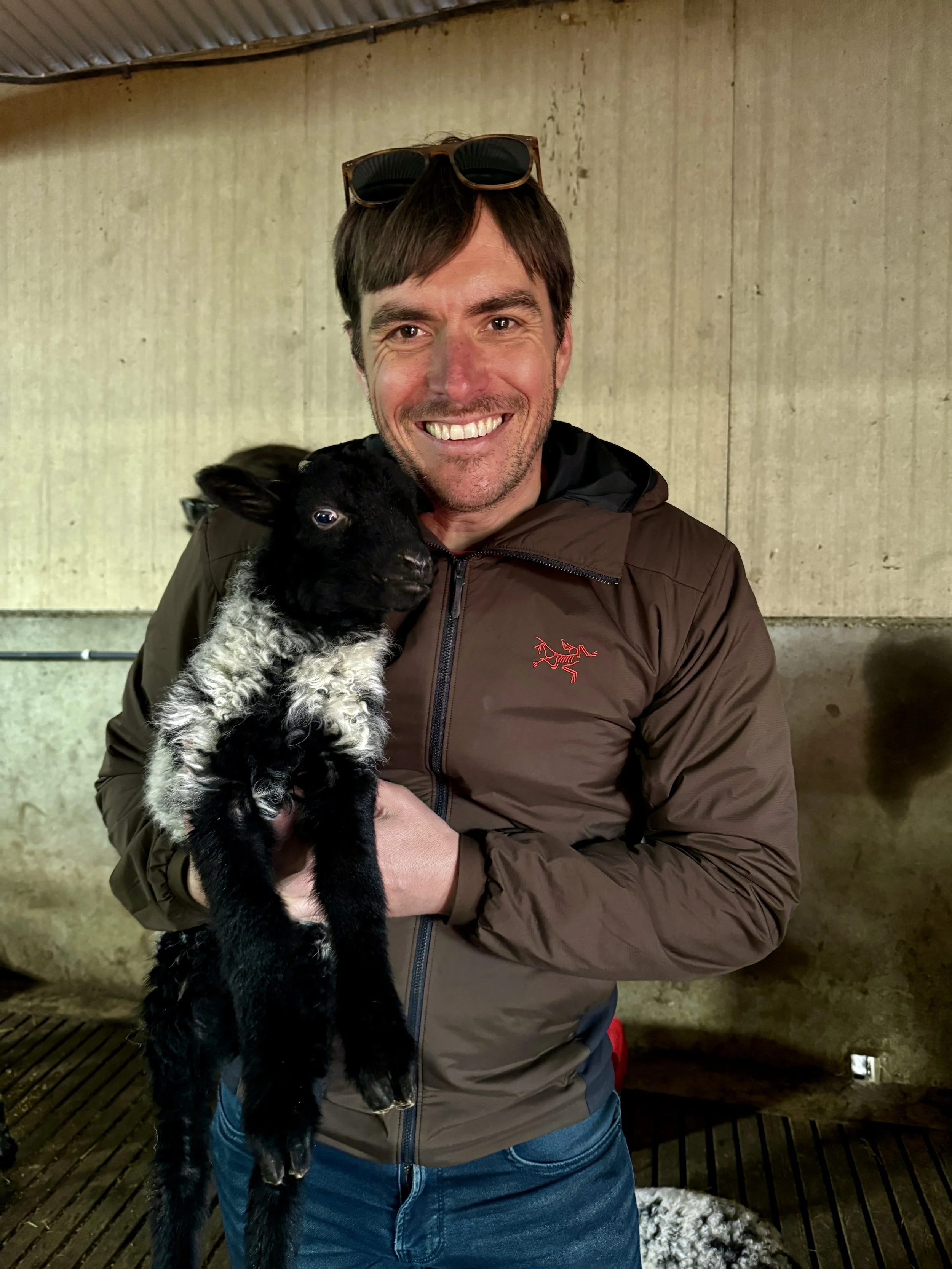A man holding a black and white puppy inside a structure with concrete walls and a wooden floor.