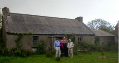 Four people standing in front of an old barn in a grassy area.
