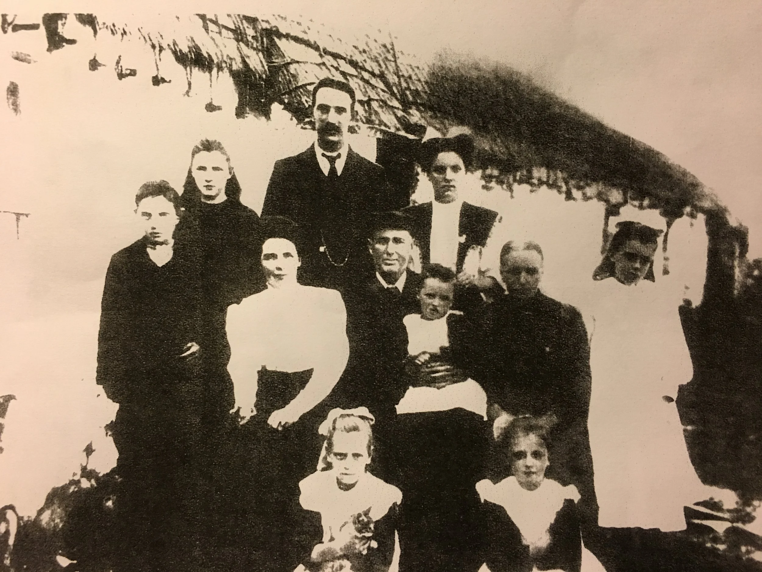Black and white photo of a group of people, some standing and some sitting, in front of a pagoda-style building with a curved roof.