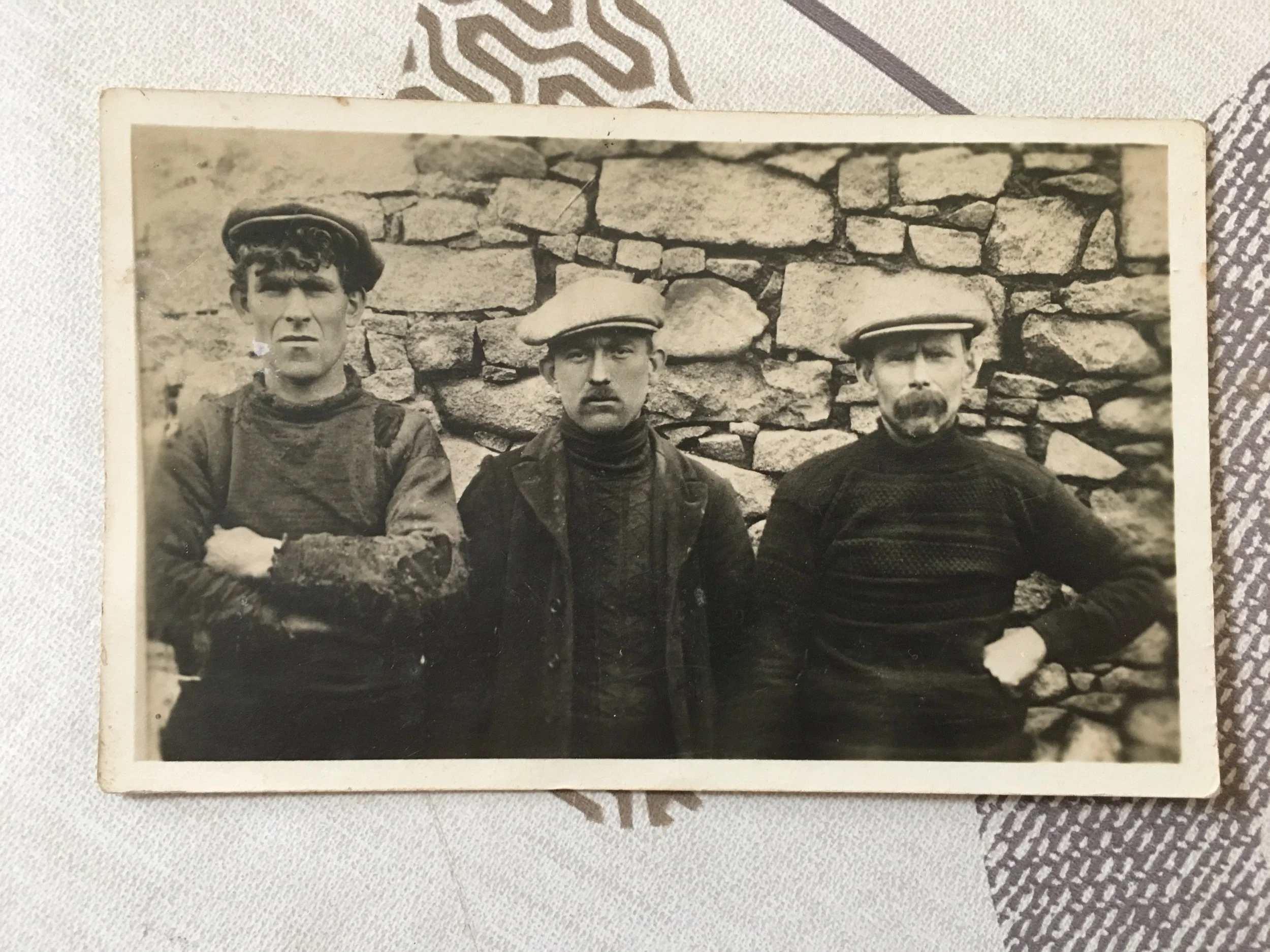A black and white vintage photo of three men standing in front of a stone wall, wearing old-fashioned hats and clothing.