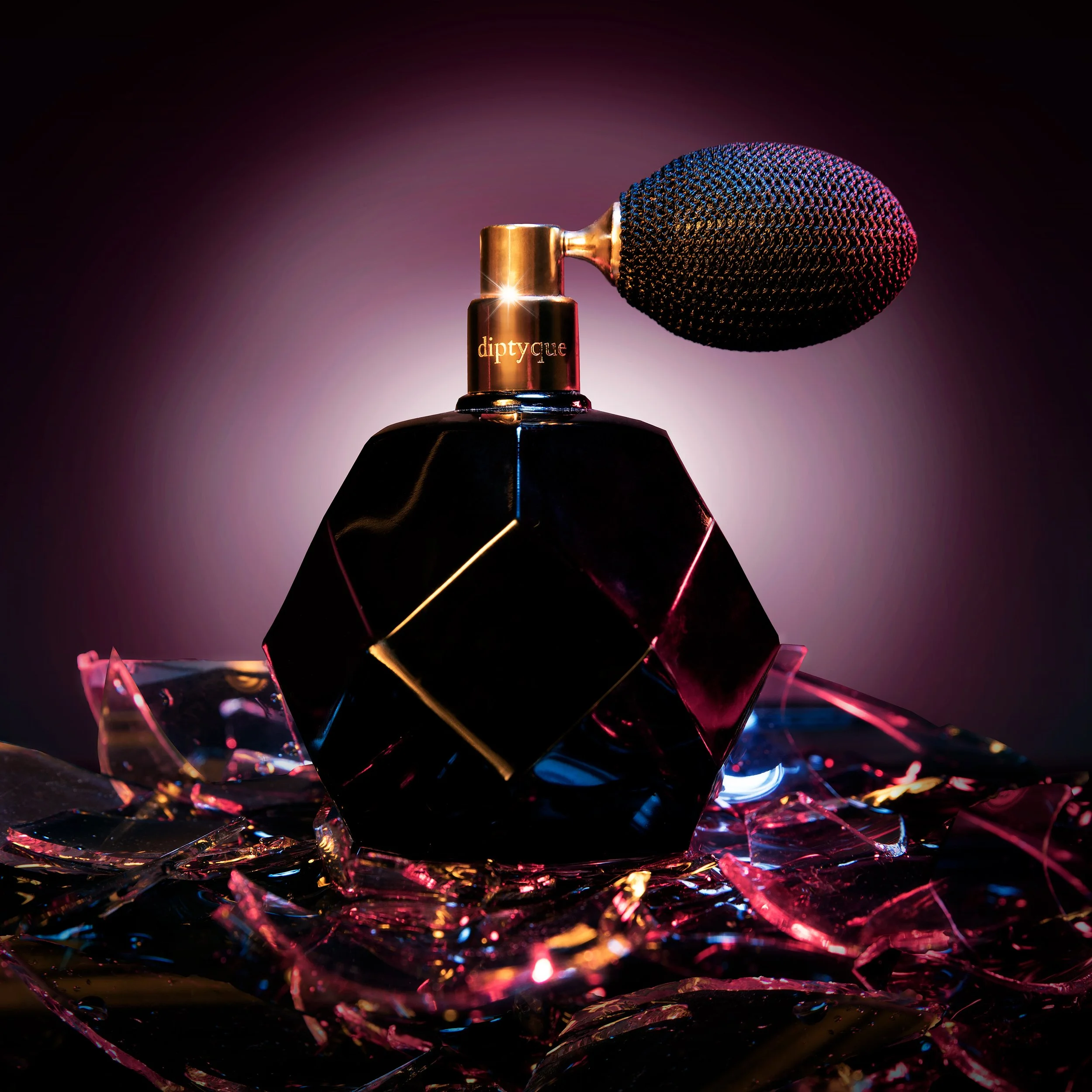 A microphone with a black mesh head and gold base, with the brand name 'diptyque' inscribed on it, positioned above a multifaceted glass object reflecting colorful lights and surrounded by a dark background.