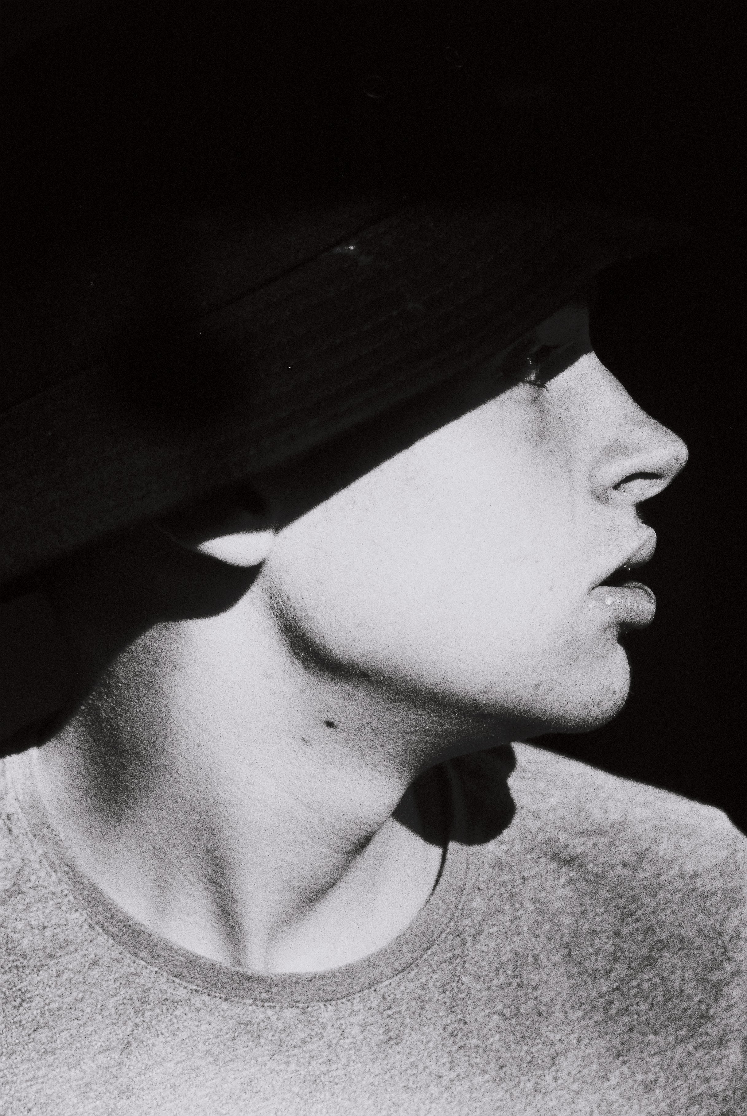Black and white photo of a woman in a bucket hat with her profile visible, taking a selfie or looking at something nearby.
