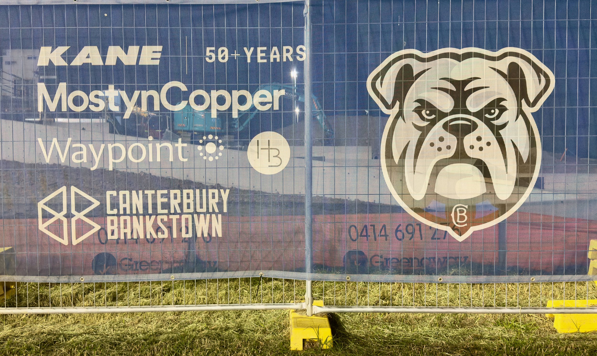 Canterbury-Bankstown Bulldogs logo and sponsor signs behind a wire fence at Belmore Sports Ground.