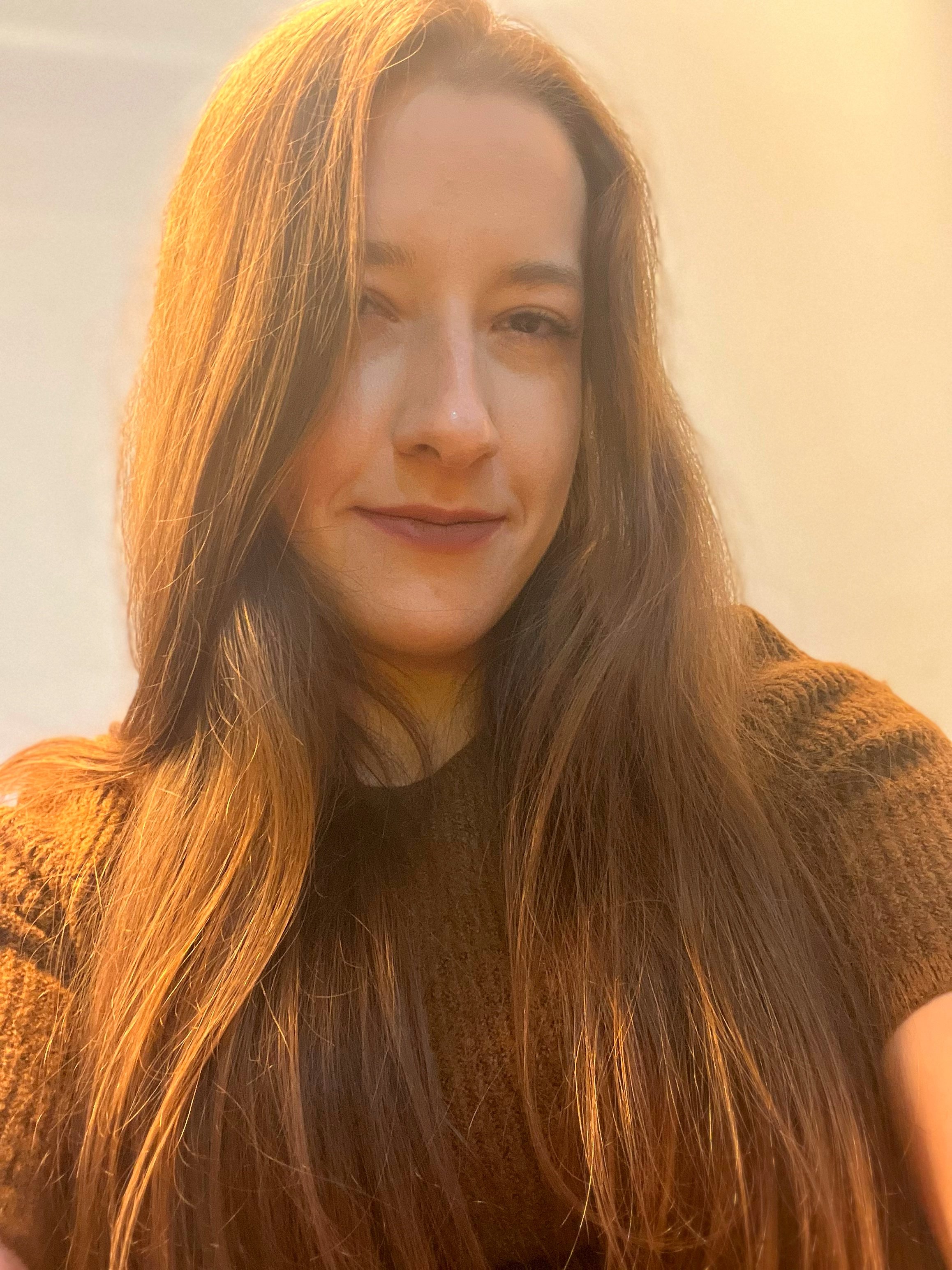 A woman with long auburn hair taking a selfie indoors with a plain background.