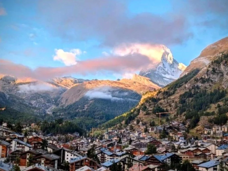 Charming mountain village with traditional houses at the foot of snow-capped mountains under a partly cloudy sky. Zermatt, Matterhorn.