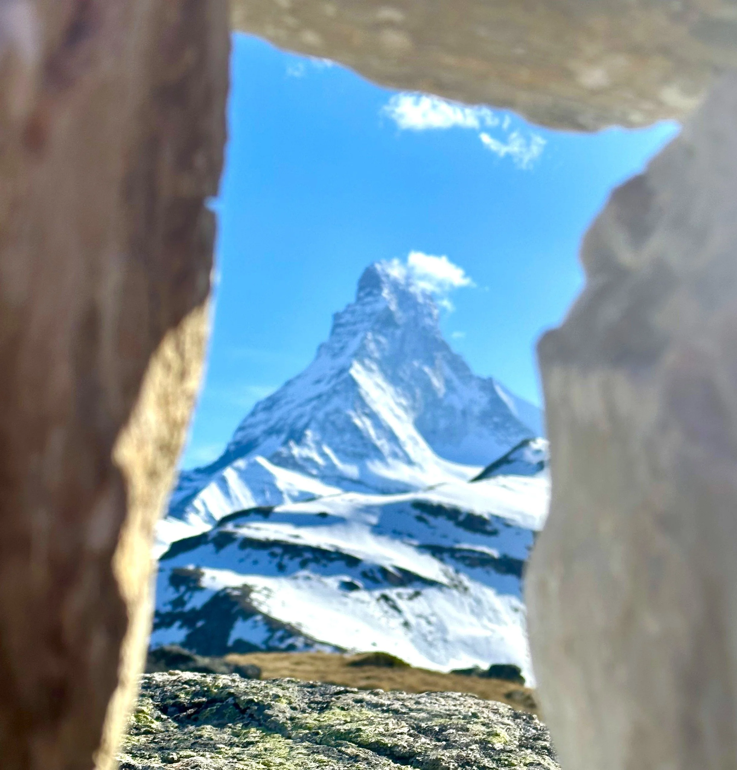 A view of snow-capped mountains under a blue sky with some clouds, seen from within a narrow rock crevice. Matterhorn, Zermatt.