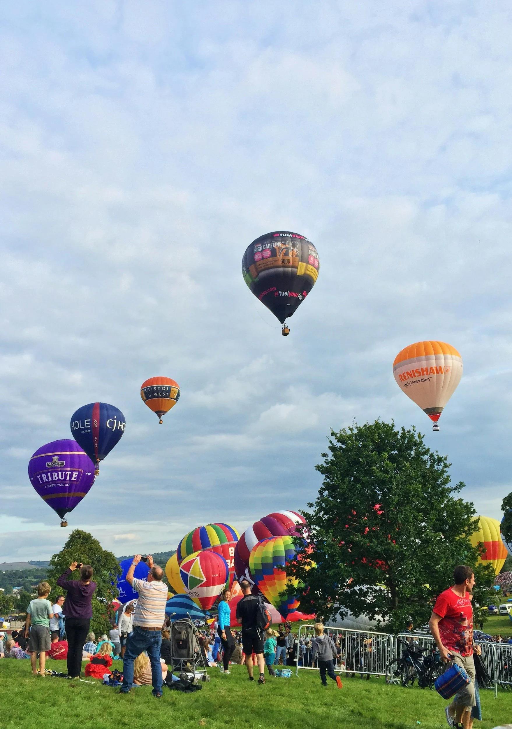 Hot air balloons being launched in the sky during a festival with people gathered on the ground watching, taking photos, and enjoying the event.