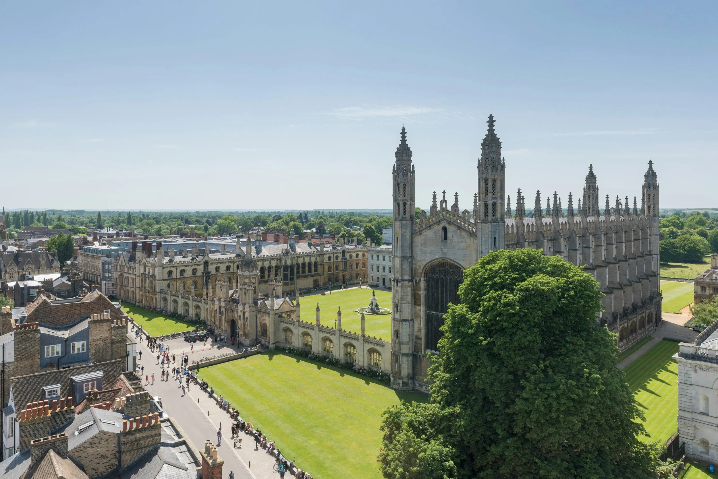 Bird's-eye view of a historic cathedral with gothic architecture, surrounded by a cityscape with buildings and a park filled with people.
