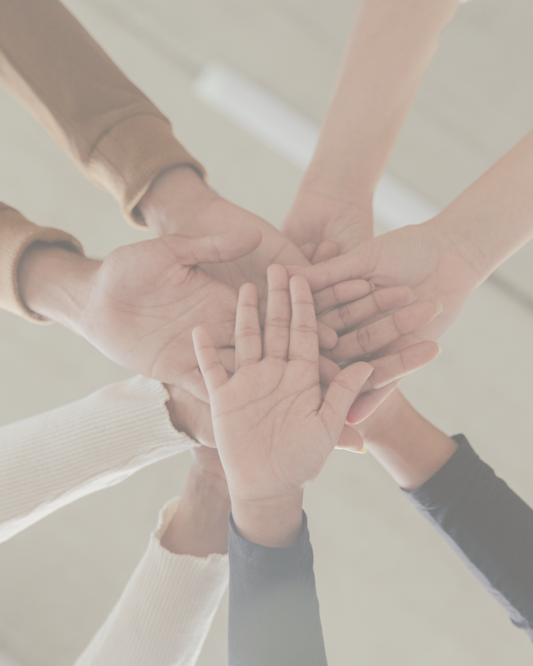 Multiple hands of different skin tones stacked together in a show of unity