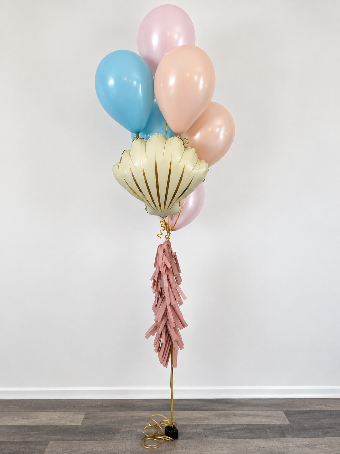 Balloons including pink, blue, cream, and shell-shaped balloons with tassels on a white background.