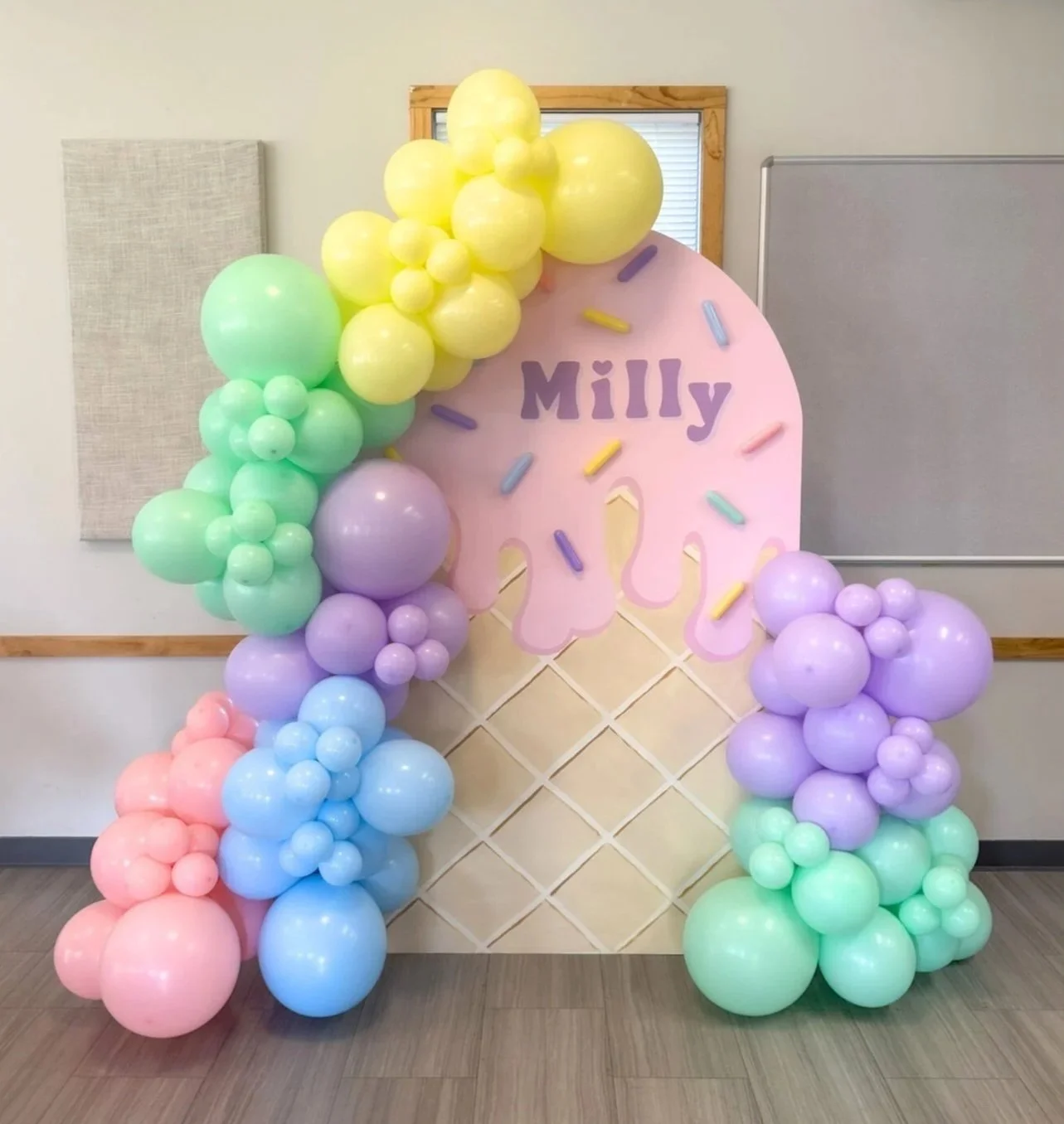 Colorful balloon display with a pink ice cream cone cutout and the name 'Milly' in purple, resembling a birthday or celebration decoration.