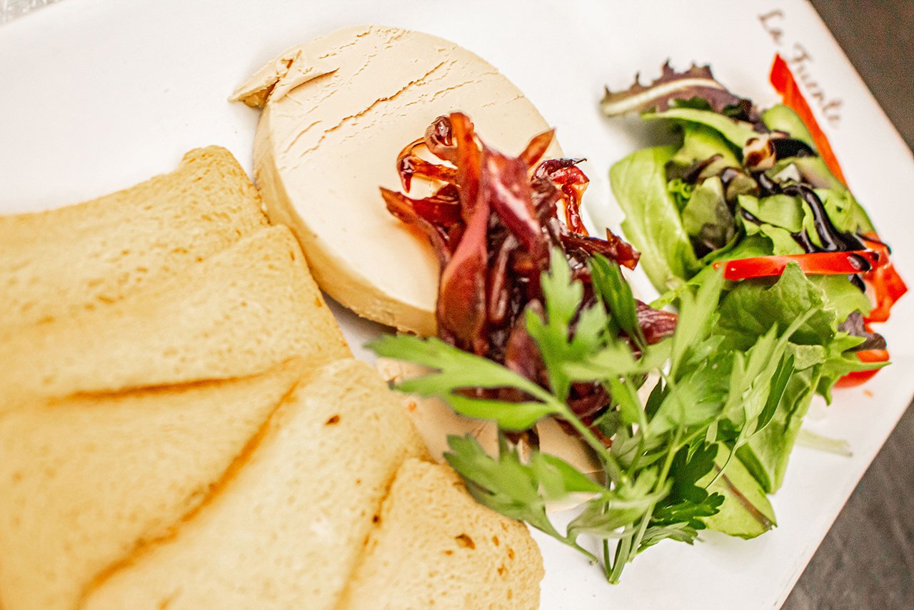 A plate with slices of bread, a round of cheese, a small portion of roasted vegetables, and a fresh salad with greens, cucumber, tomato, and red pepper strips.