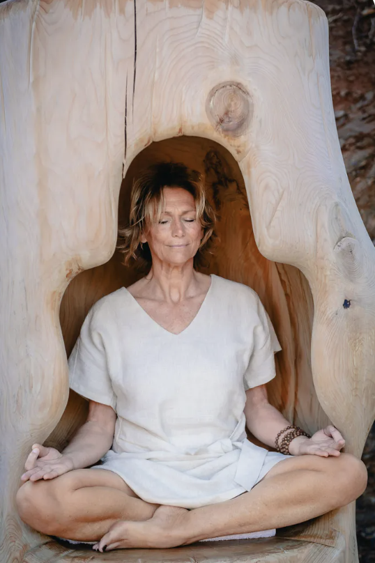 A woman practicing meditation inside a hollowed-out wooden sculpture with natural wood grain and knots visible.