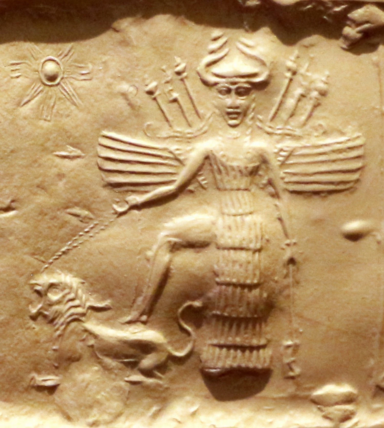 Close-up of a golden coin featuring a detailed engraving of a female figure with wings, holding a branch and wearing a headdress, surrounded by other partly visible symbols and figures.