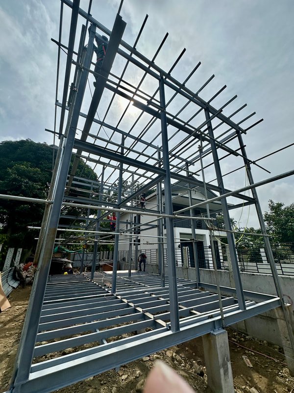 Construction site with steel framework of a building under development, showing scaffolding and partly built structure against cloudy sky.
