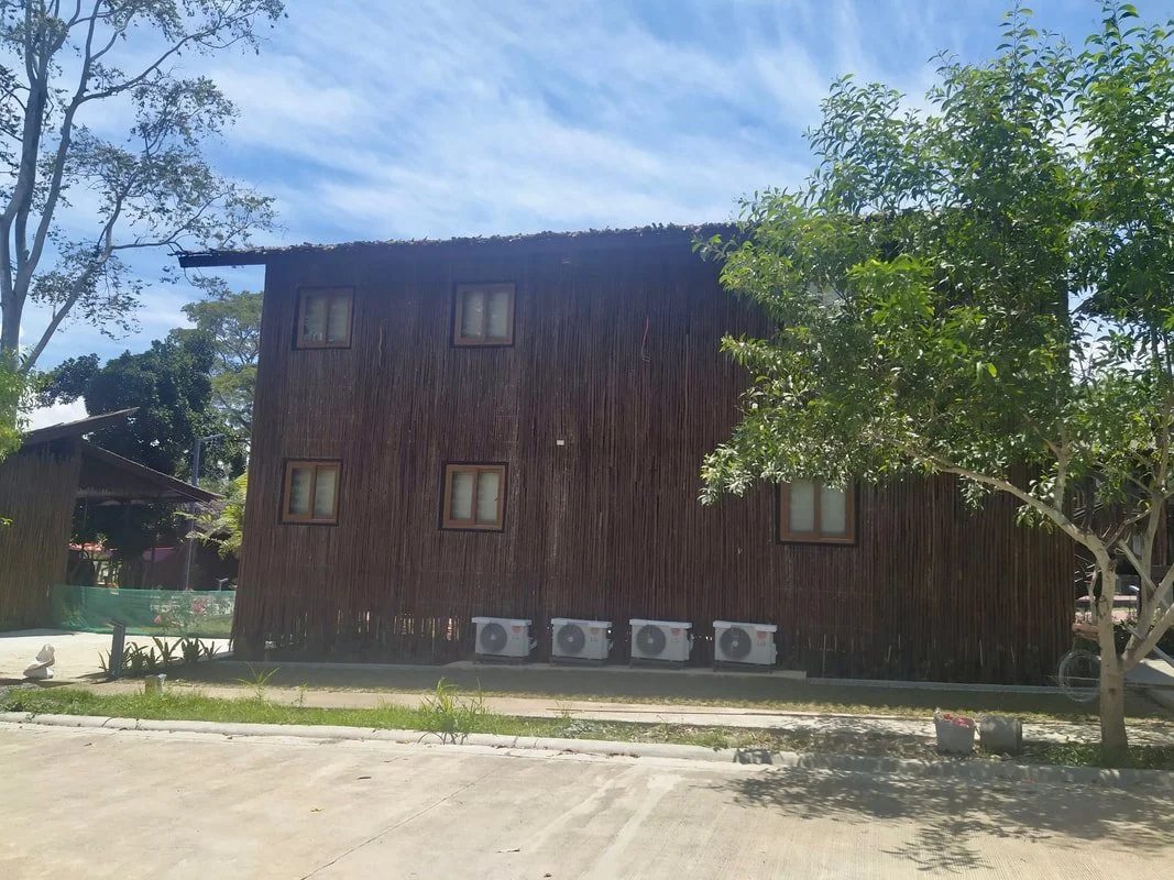 A wooden building with five air conditioning units at its base, surrounded by trees and a partly cloudy sky.