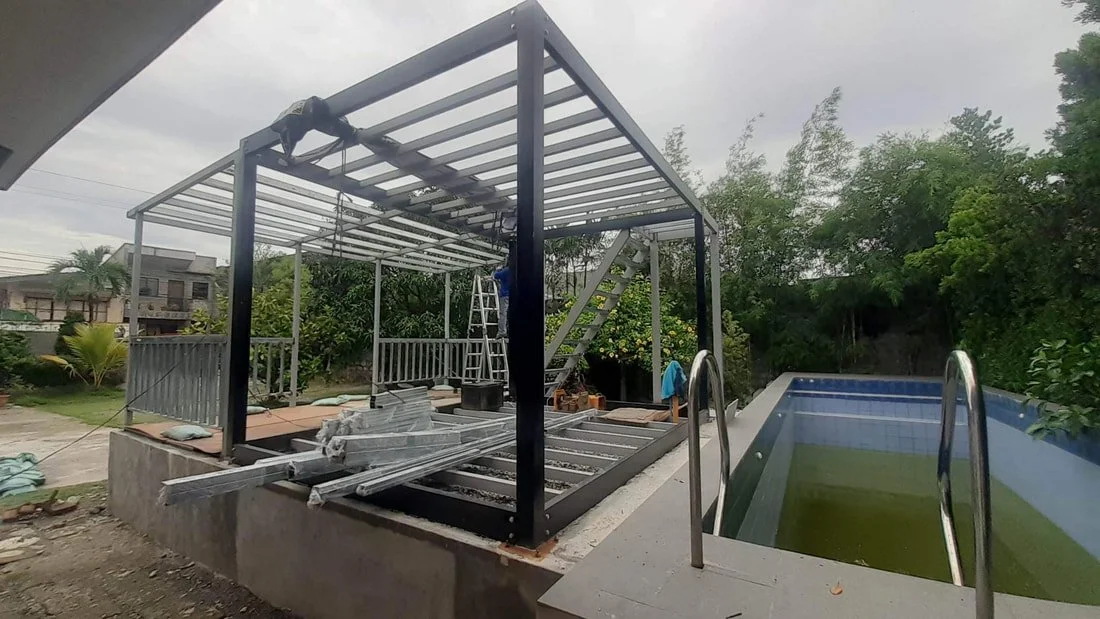Construction of a poolhouse or outdoor structure near a swimming pool, with scaffolding, ladders, and building materials visible.