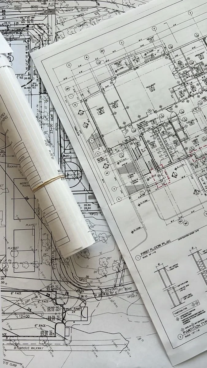 Architectural blueprints and detailed construction plans for a building project, with rolled-up plans and a pen on top.