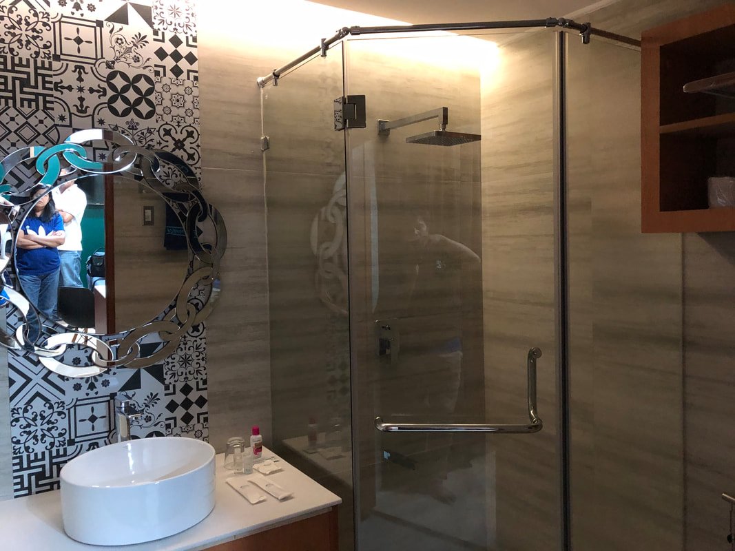 Modern bathroom with patterned black and white wall tiles, a decorative mirror, a white vessel sink on a countertop with toiletries, and a glass shower enclosure with wood-tone wall panels.