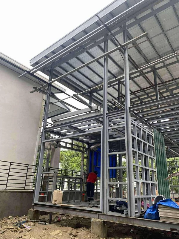 Construction site with metal framework and partially roofed structure, worker installing or inspecting infrastructure.