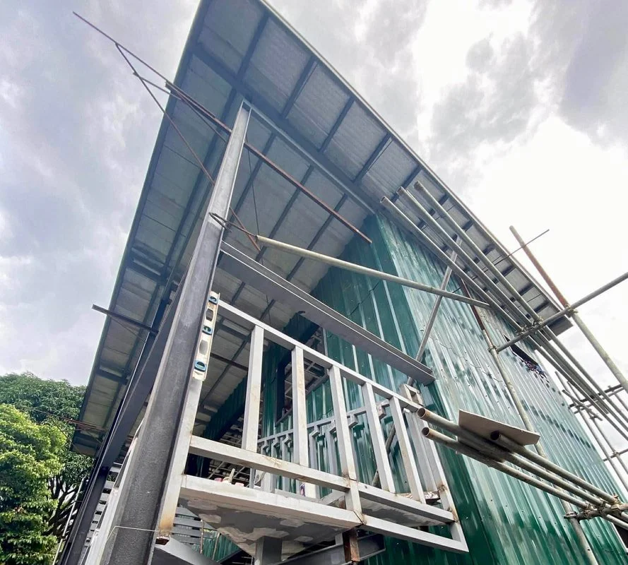 Under construction building with metal framing, scaffolding, and a roof, viewed from below.