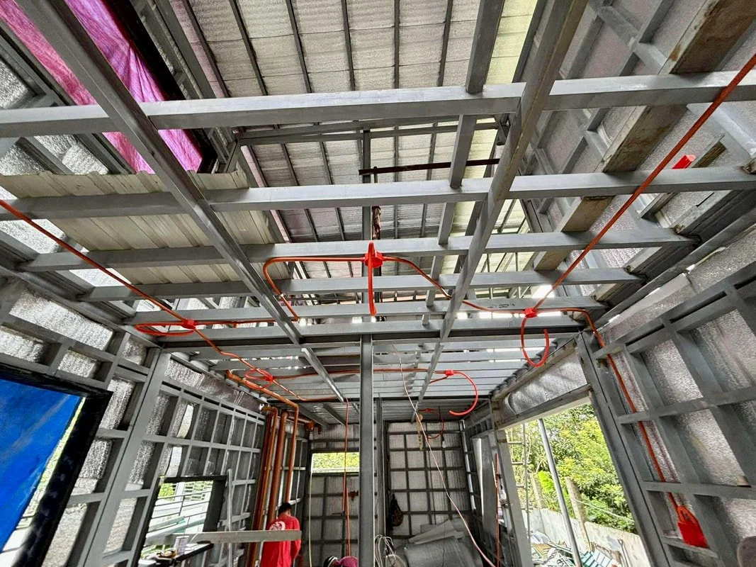 Construction site with an incomplete building frame, exposed steel studs, and orange electrical conduit wiring.