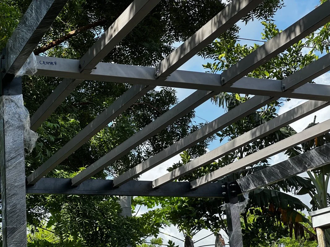 Construction of a metal frame structure outdoors with trees and a blue sky in the background.