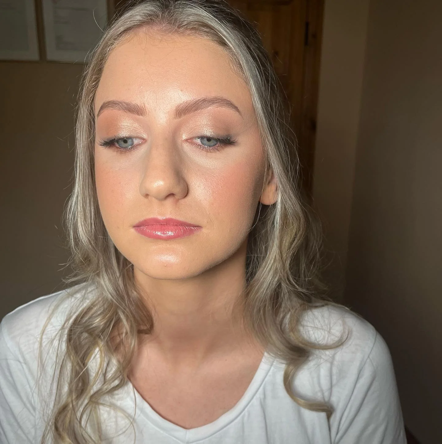 Close-up of a young woman with blonde wavy hair, fair skin, light makeup, and a white top, looking slightly to the side with a neutral expression.