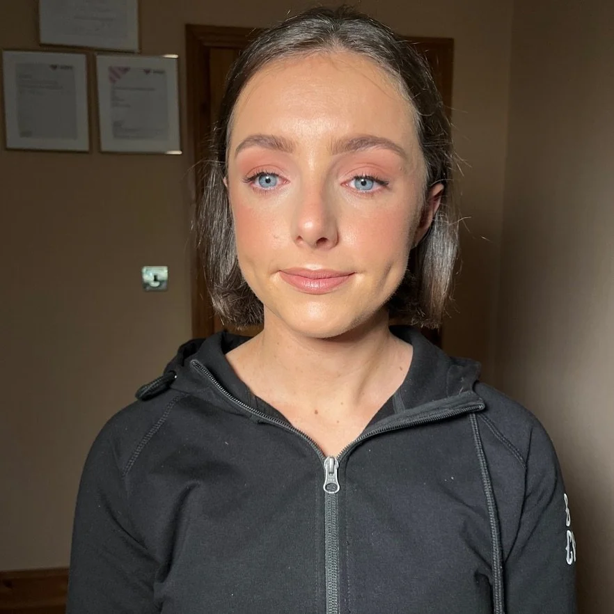 Young woman with shoulder-length brown hair and blue eyes, wearing a black zip-up hoodie, standing indoors with a neutral expression.