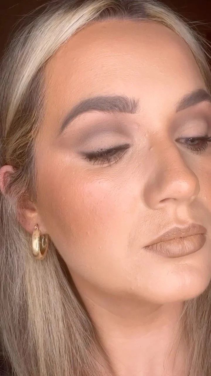 Close-up of a woman with blonde hair, wearing gold hoop earrings and makeup, looking slightly downward with closed eyes.
