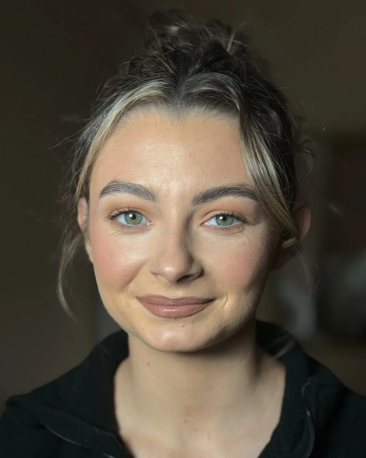 Close-up portrait of a smiling woman with light skin, blue eyes, and dark hair pulled up, wearing a black top in Dingle, Kerry.