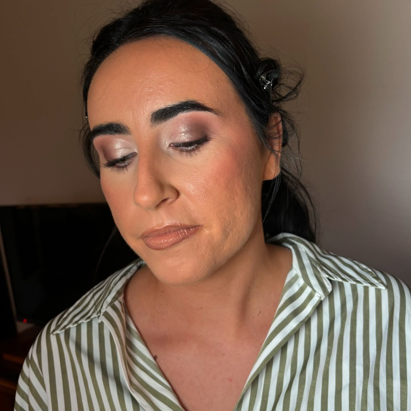 A woman with dark hair, makeup, and a striped shirt looking down with a neutral expression.